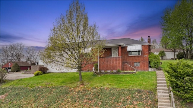 view of front of home with a chimney, brick siding, and a lawn