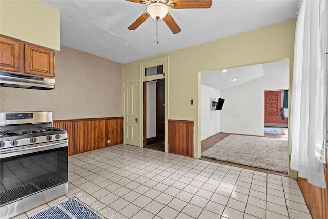 1310 Diana St, Spring Hill, PA 15212 - kitchen with brown cabinets, under cabinet range hood, stainless steel range with gas cooktop, ceiling fan, and a wainscoted wall
