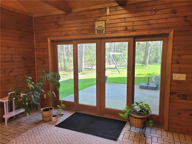 doorway to outside with wood walls, vaulted ceiling with beams, brick floor, and plenty of natural light