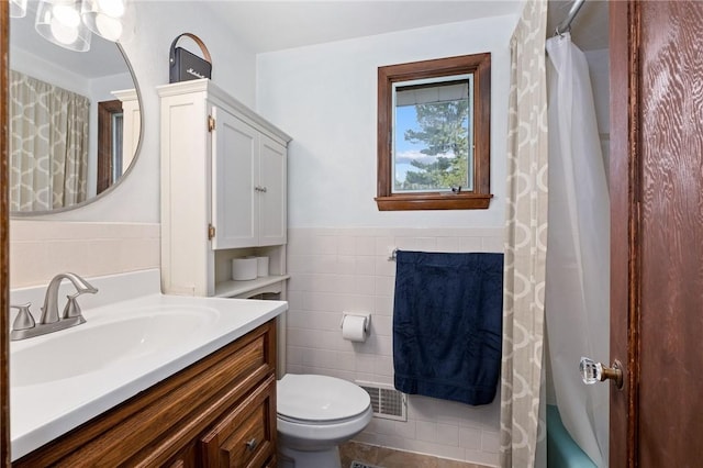 full bath featuring visible vents, tile walls, wainscoting, vanity, and toilet