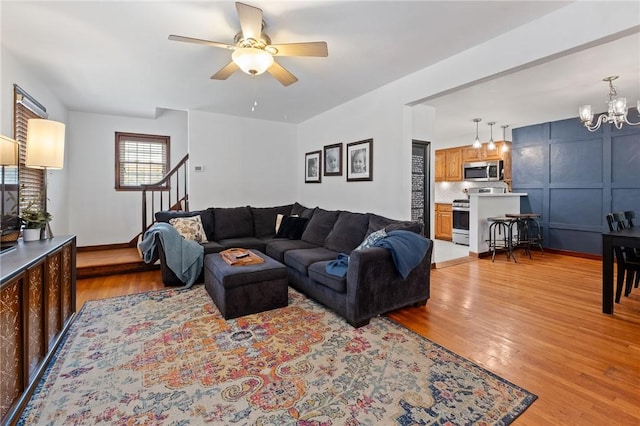 living area with baseboards, stairway, light wood-style flooring, and ceiling fan with notable chandelier