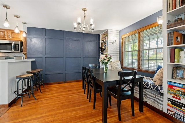 dining area with a chandelier, light wood-style flooring, and a decorative wall
