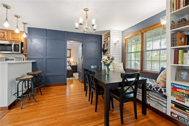 dining space featuring an inviting chandelier, light wood-style flooring, and a decorative wall