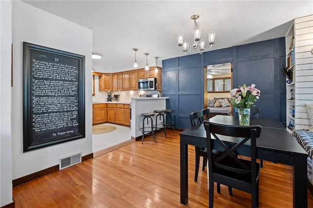 dining area with visible vents, light wood-style flooring, ceiling fan with notable chandelier, and baseboards