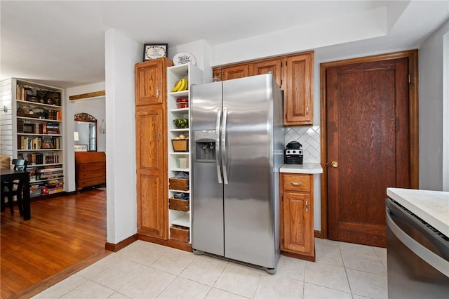 kitchen featuring light countertops, brown cabinetry, stainless steel appliances, and open shelves