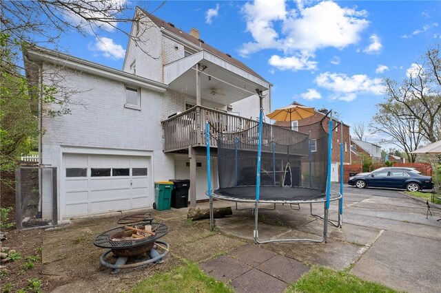 back of property with a trampoline, an attached garage, brick siding, a wooden deck, and ceiling fan
