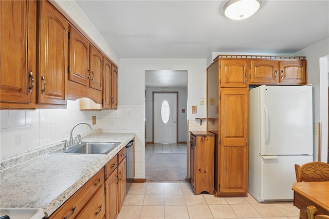 kitchen with freestanding refrigerator, light countertops, brown cabinets, a sink, and light tile patterned floors