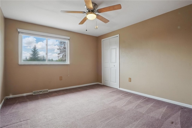 carpeted spare room with visible vents, baseboards, and ceiling fan