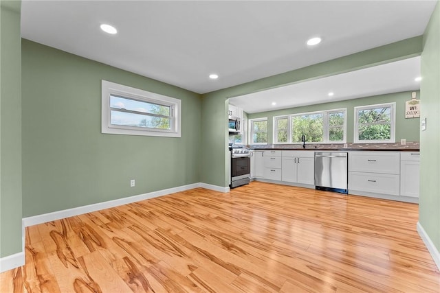 kitchen with a healthy amount of sunlight, appliances with stainless steel finishes, light wood finished floors, and dark countertops