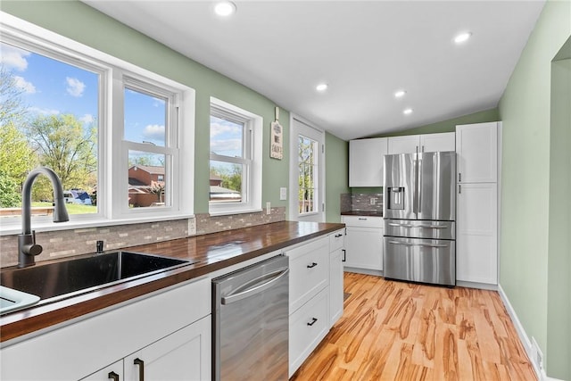 kitchen with tasteful backsplash, a sink, white cabinets, stainless steel appliances, and light wood-style flooring