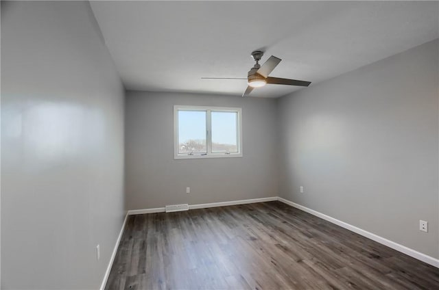 empty room featuring dark wood-style flooring, ceiling fan, visible vents, and baseboards
