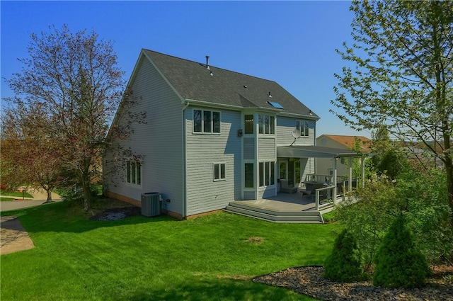 back of property with a lawn, roof with shingles, central AC unit, and a deck