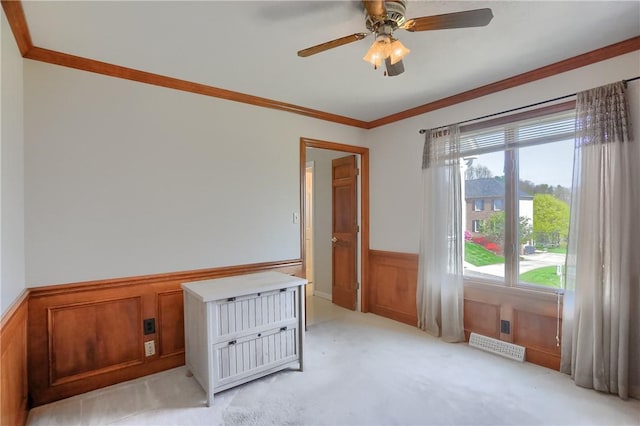 unfurnished room with plenty of natural light, crown molding, light carpet, and a wainscoted wall