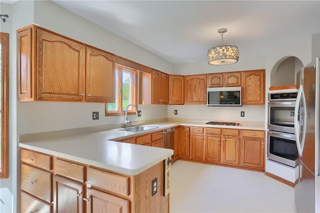 kitchen with a peninsula, light countertops, a sink, hanging light fixtures, and stainless steel appliances
