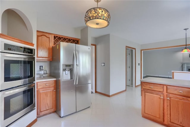 kitchen featuring brown cabinetry, pendant lighting, appliances with stainless steel finishes, light countertops, and baseboards