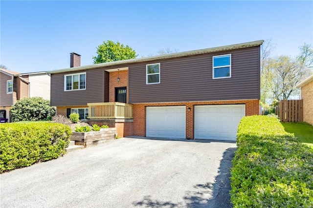 raised ranch with a chimney, brick siding, fence, aphalt driveway, and an attached garage