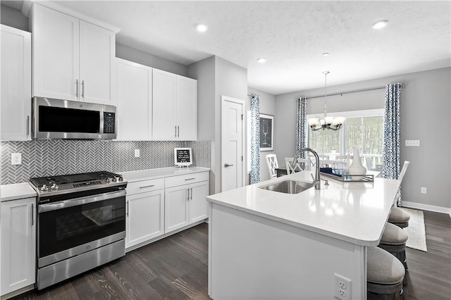 kitchen with a sink, stainless steel appliances, dark wood finished floors, and a chandelier