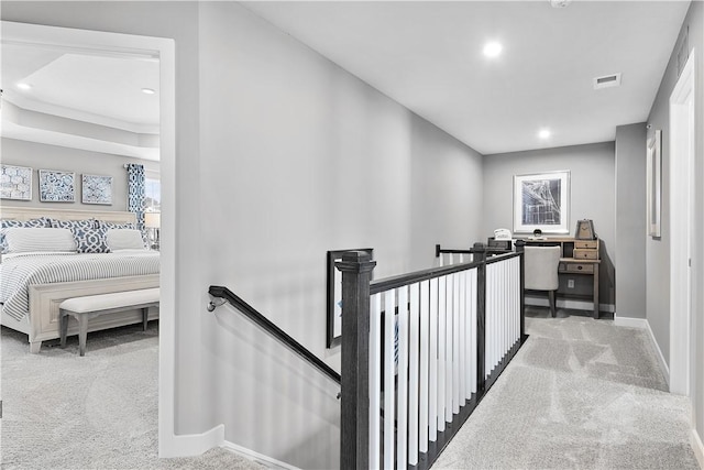 hallway with carpet floors, baseboards, visible vents, and an upstairs landing