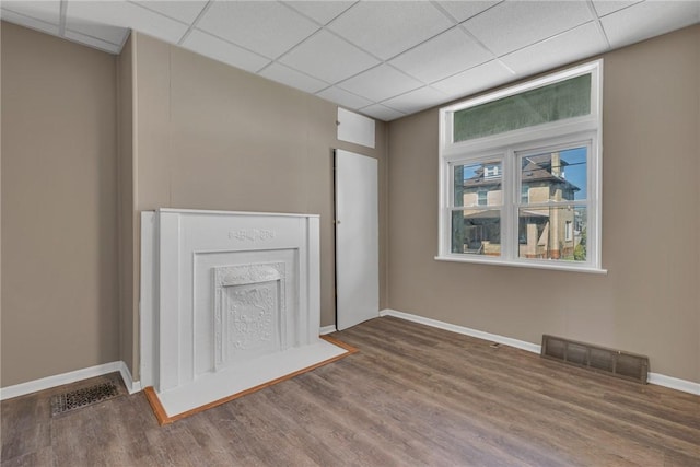 unfurnished living room with visible vents, baseboards, a drop ceiling, and wood finished floors