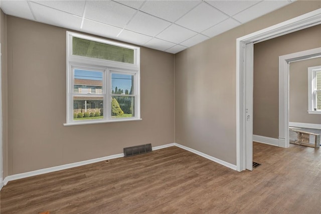 unfurnished room with a healthy amount of sunlight, a paneled ceiling, visible vents, wood finished floors, and baseboards