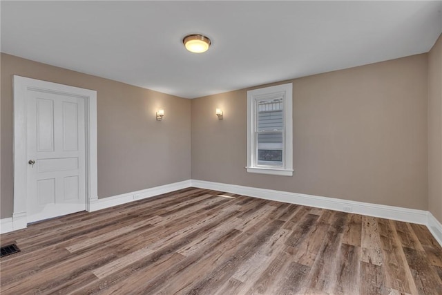 empty room featuring baseboards, wood finished floors, and visible vents