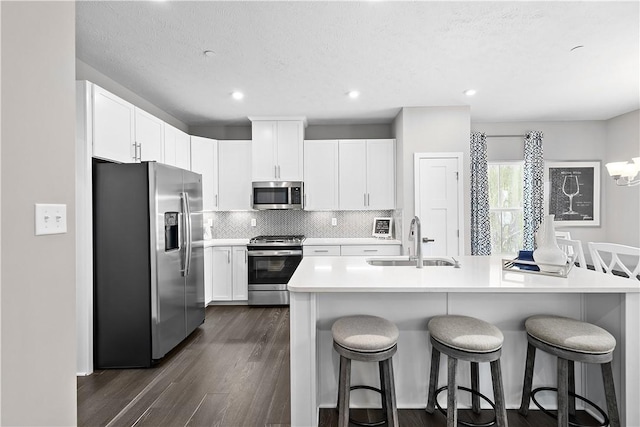 kitchen with a breakfast bar area, stainless steel appliances, a sink, and dark wood-type flooring