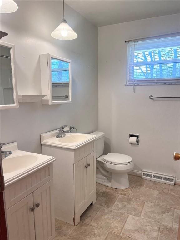 bathroom with toilet, visible vents, two vanities, and a sink