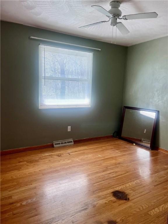 unfurnished room with baseboards, ceiling fan, visible vents, and light wood-style flooring