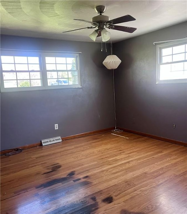empty room with a healthy amount of sunlight, a ceiling fan, wood finished floors, and visible vents