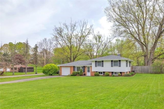 tri-level home with a chimney, a front yard, fence, aphalt driveway, and an attached garage