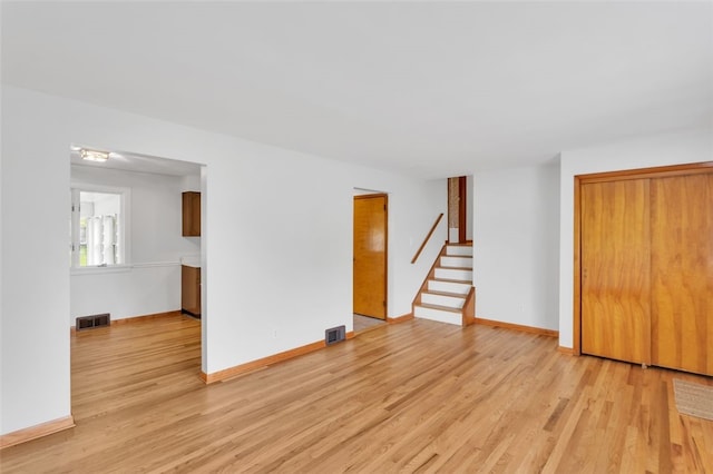 unfurnished living room with visible vents, light wood finished floors, baseboards, and stairway