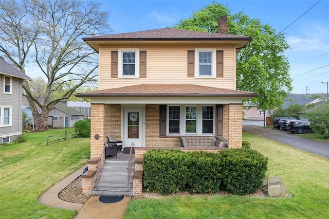 american foursquare style home with covered porch, brick siding, a chimney, and a front yard