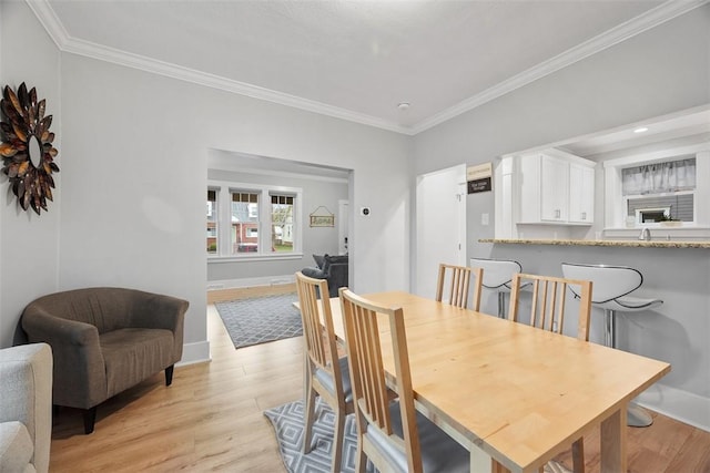 dining space featuring crown molding, light wood-style floors, and baseboards