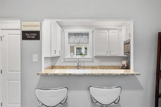 kitchen featuring a sink, light stone counters, white cabinets, and stainless steel microwave