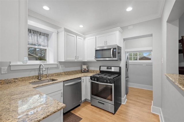 kitchen featuring light stone countertops, a sink, light wood-style floors, stainless steel appliances, and white cabinetry