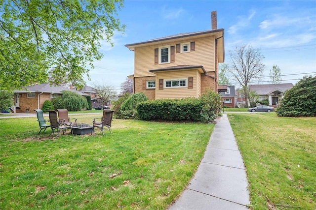 back of property featuring a chimney, a yard, a fire pit, and brick siding