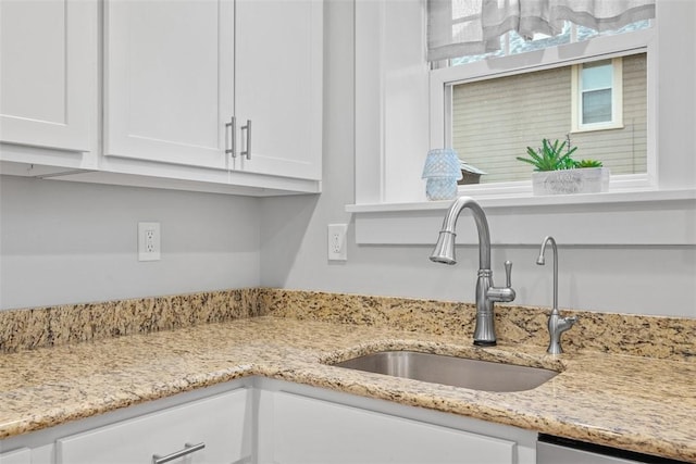 room details with a sink, light stone counters, stainless steel dishwasher, and white cabinetry
