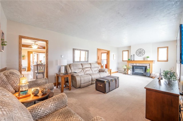 carpeted living area featuring ceiling fan, a baseboard heating unit, a healthy amount of sunlight, and a fireplace