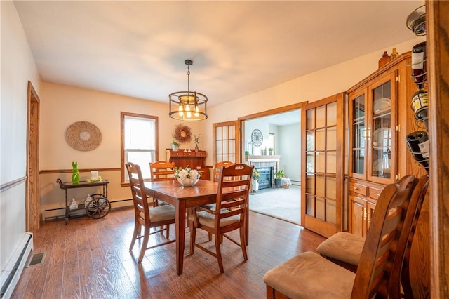 dining room featuring baseboards, dark wood-style flooring, a baseboard heating unit, and a chandelier