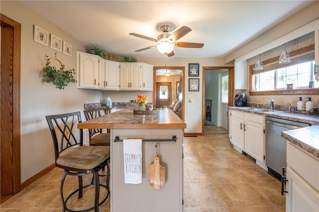 kitchen with a kitchen breakfast bar, a ceiling fan, stainless steel dishwasher, a sink, and white cabinets