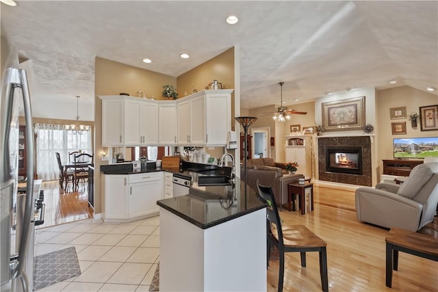 kitchen featuring a peninsula, open floor plan, white cabinetry, a sink, and ceiling fan with notable chandelier