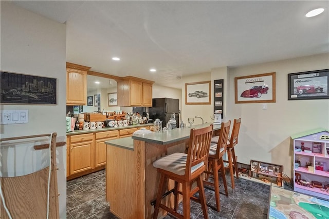 kitchen featuring recessed lighting, freestanding refrigerator, light brown cabinets, and a breakfast bar