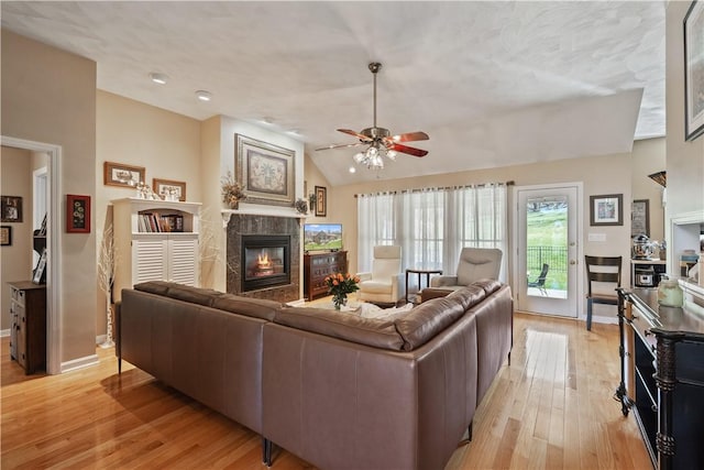 living room featuring ceiling fan, a fireplace, light wood-type flooring, baseboards, and lofted ceiling