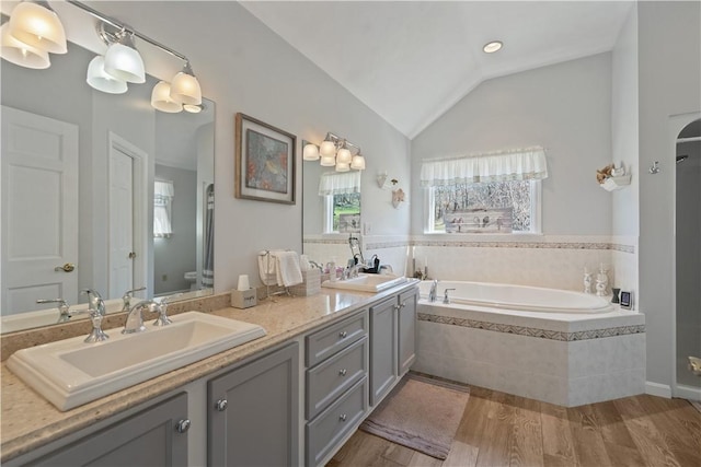 bathroom with a sink, double vanity, toilet, wood finished floors, and a bath