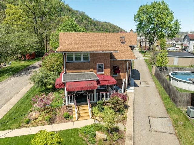view of front of house featuring fence, roof with shingles, a chimney, brick siding, and driveway
