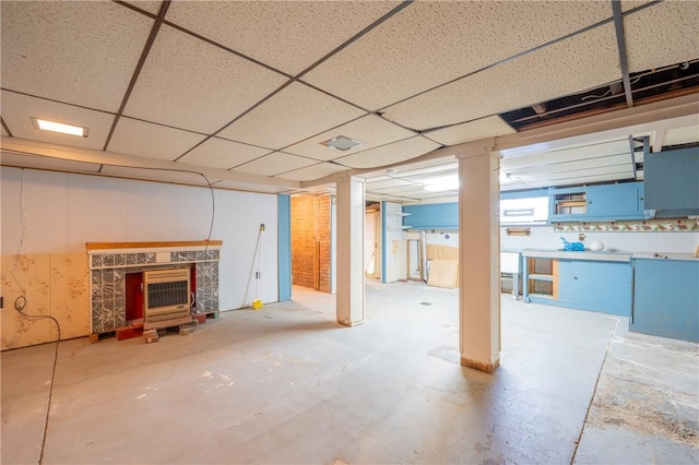 basement featuring a drop ceiling and a wood stove
