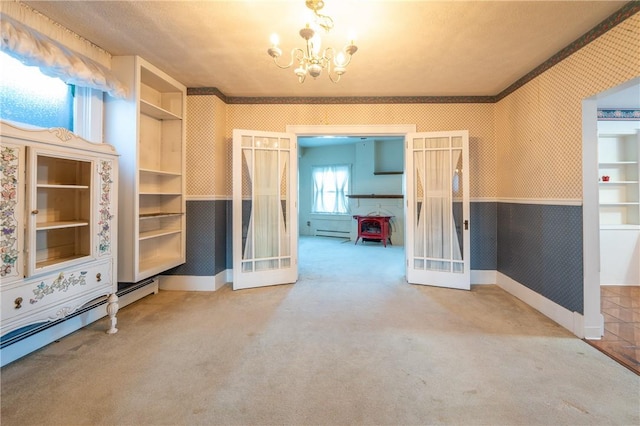 carpeted empty room with an inviting chandelier, baseboards, wainscoting, and wallpapered walls