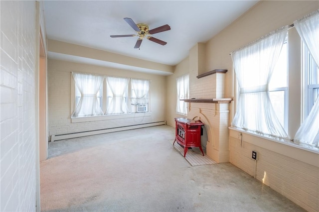 carpeted spare room with a wood stove, ceiling fan, and a baseboard heating unit