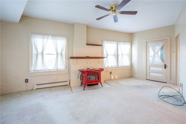 carpeted living area featuring a baseboard radiator, a ceiling fan, brick wall, and a wood stove