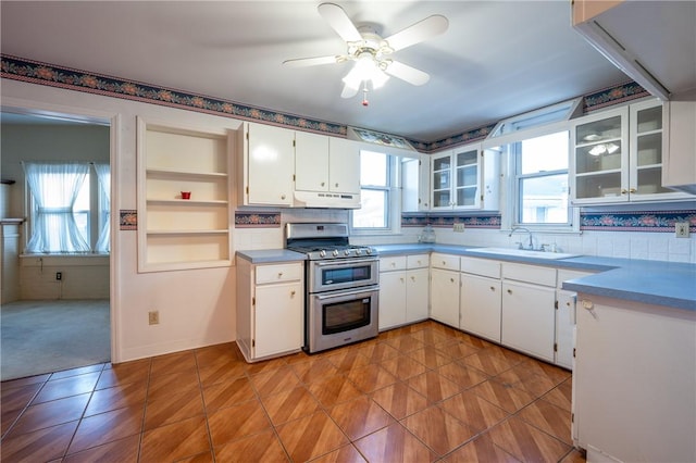 kitchen featuring under cabinet range hood, white cabinets, range with two ovens, a sink, and light tile patterned floors
